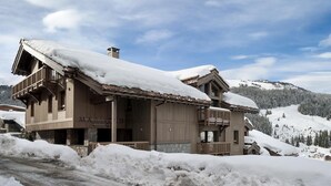 Una cabaña de madera con balcón y cimientos de piedra, rodeada de montañas nevadas.