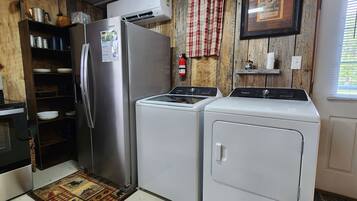 A compact kitchen with a refrigerator, washer, dryer, and a small shelf with items.