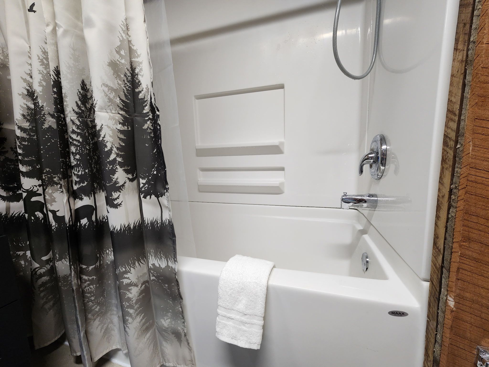 A bathroom with a bathtub, a shower, and a curtain with a forest print.