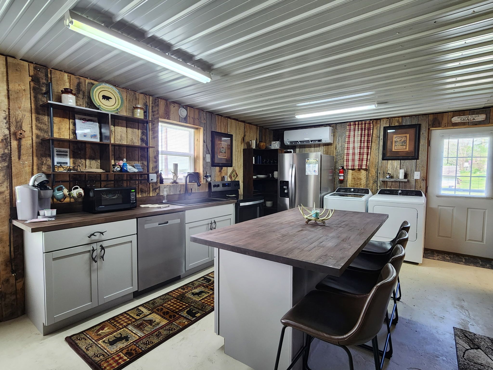 A kitchen with a central island, bar stools, stainless steel appliances, and a rustic wooden wall.