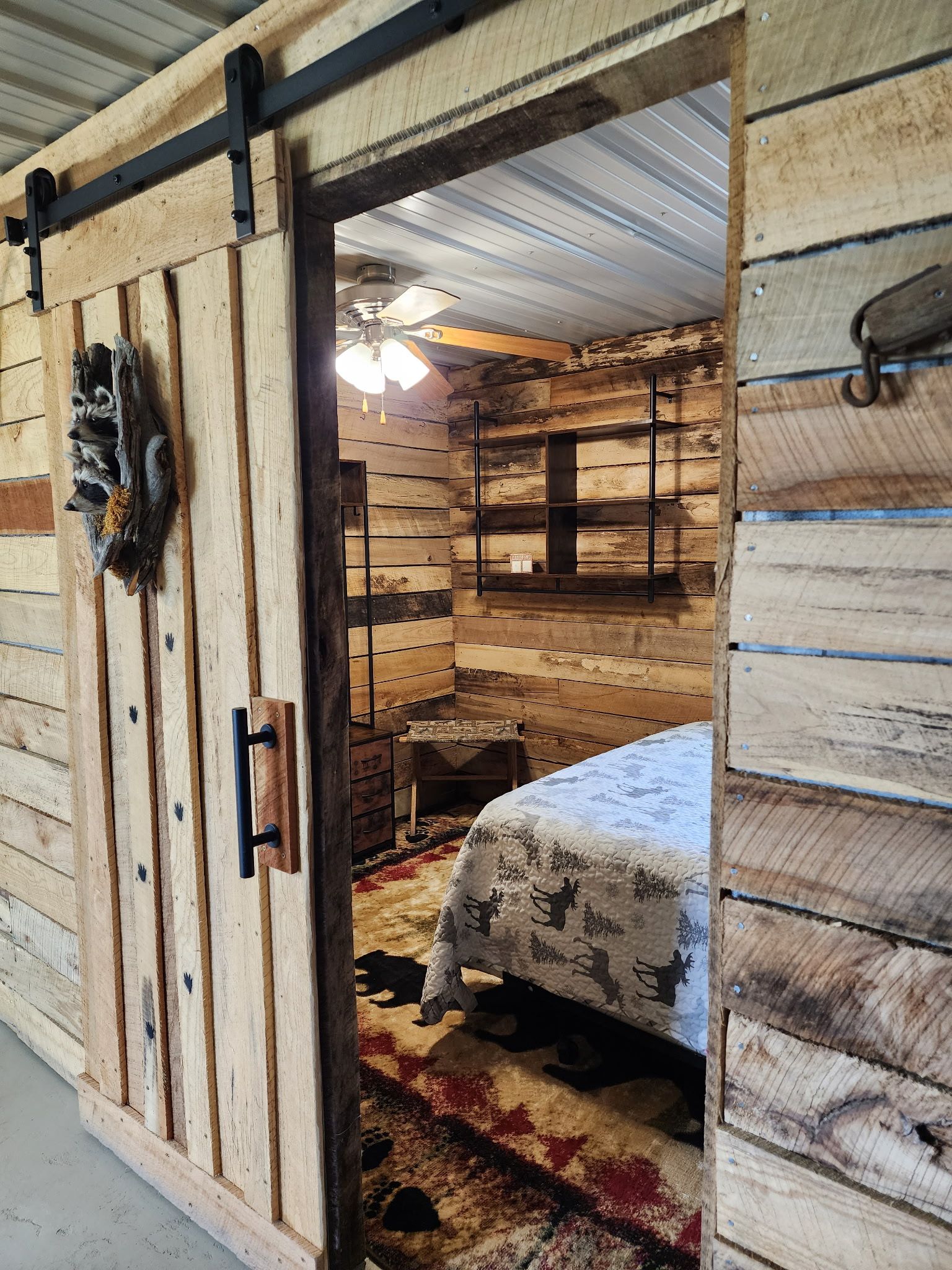 Um quarto rústico de madeira com uma cama, um ventilador de teto e uma porta de madeira.