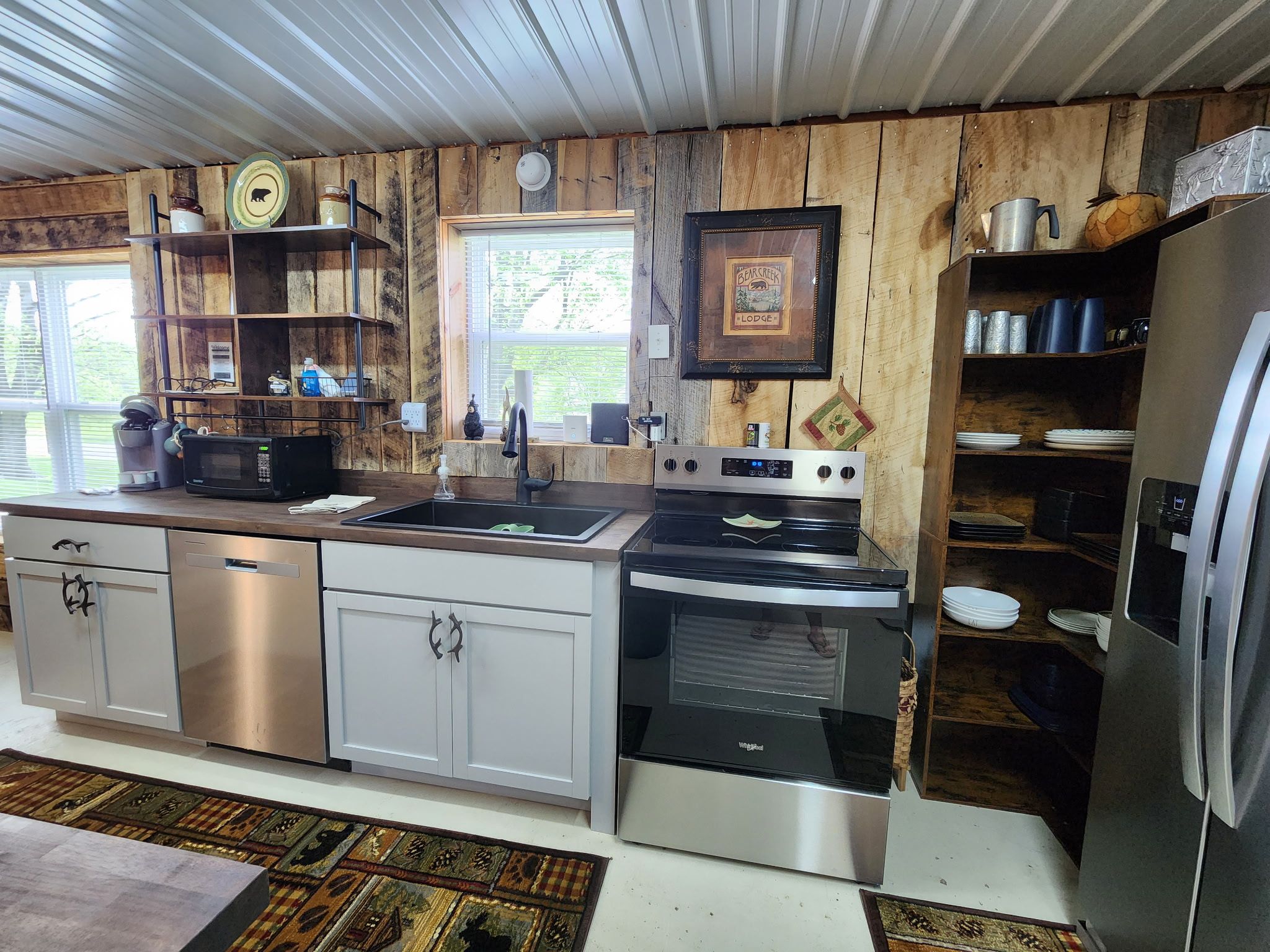 A kitchen with stainless steel appliances, wooden walls, and a window providing natural light.