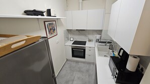 Een kleine keuken met witte kastjes, een roestvrijstalen koelkast, een inbouwoven en een koffieapparaat.