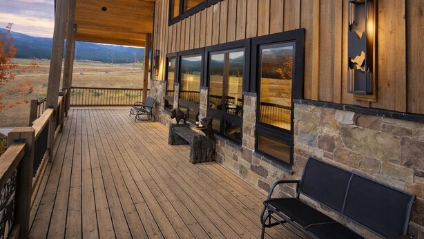A wooden deck with a bench, stone accents, and large windows overlooking a landscape.