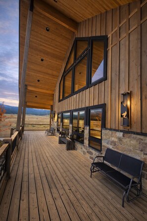Une terrasse en bois avec un banc, des éléments décoratifs en pierre et de grandes fenêtres donnant sur un paysage.