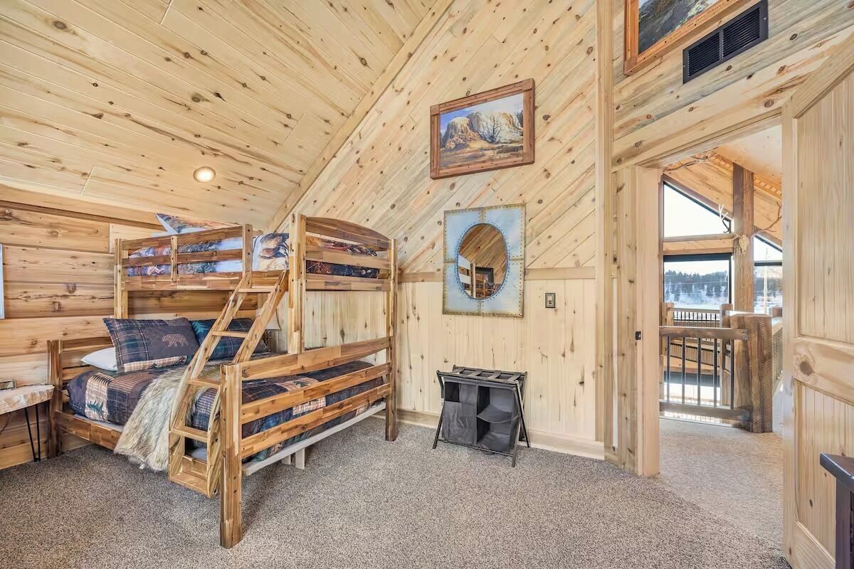 A wooden cabin interior with bunk beds, a small table, and a window with a view.