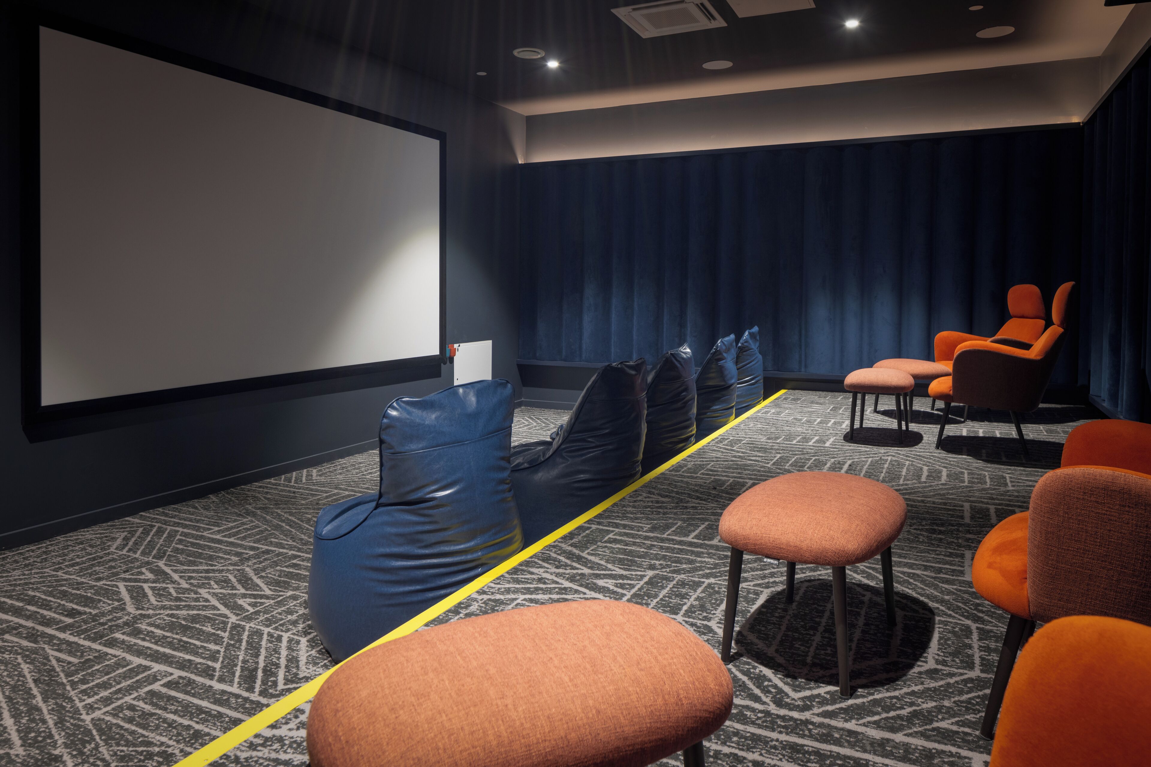 Une salle de cinéma dotée d’un grand écran, de rangées de sièges et d’un tapis à motifs.