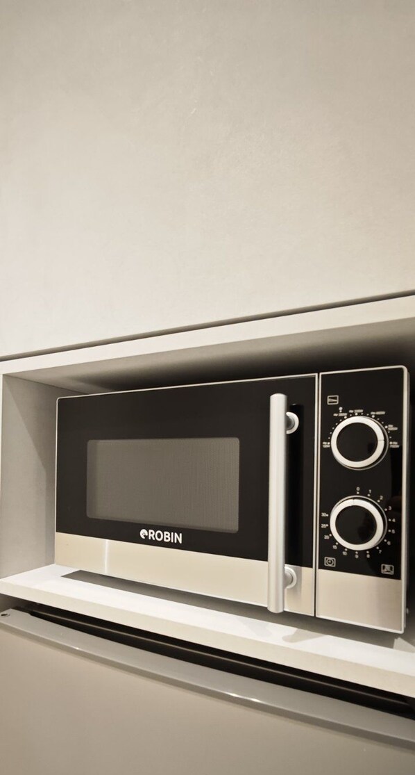 A modern microwave oven with a digital display and control panel, placed on a white countertop.