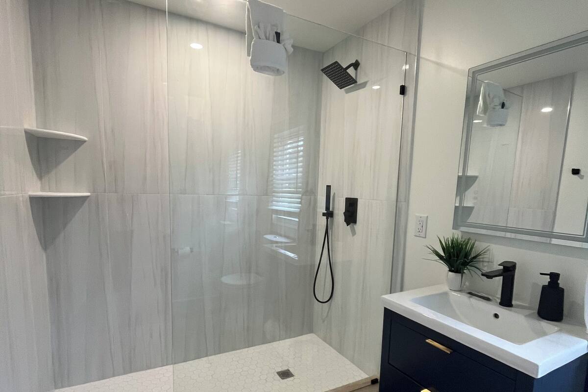 A modern bathroom with a glass-enclosed shower, a vanity with a sink, and a mirror.