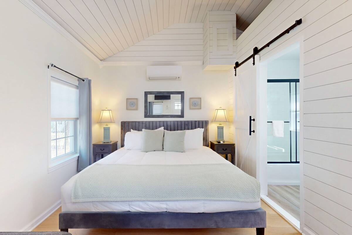 A bedroom with a bed, bedside lamps, a mirror, and a sliding door leading to a bathroom.