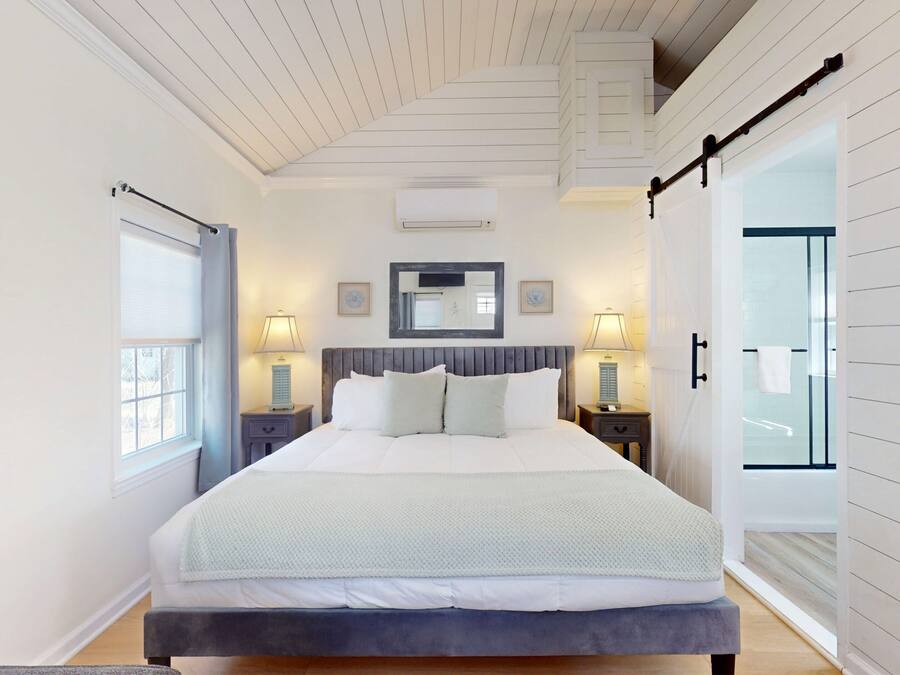 Un dormitorio con cama, lámparas de noche, un espejo y una puerta corrediza que da al baño.
