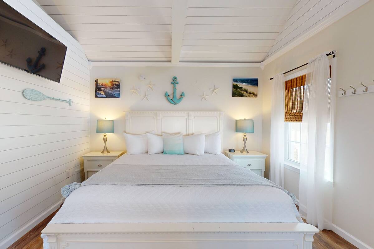 A bedroom with a large bed, two bedside tables with lamps, a ceiling fan, and nautical-themed decor.