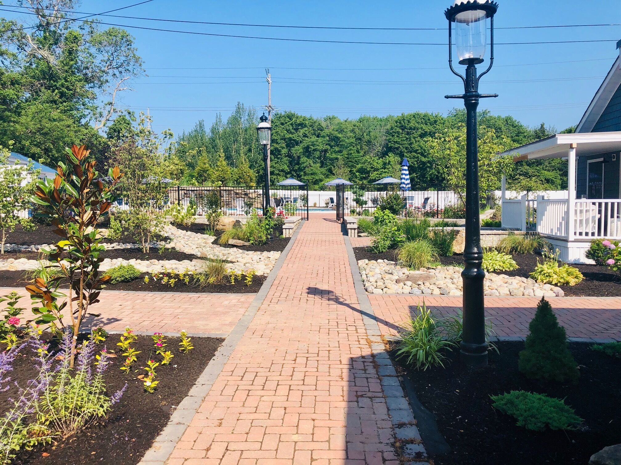 A brick pathway leading to a gazebo, surrounded by landscaped gardens and a white fence.