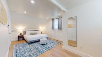 A bedroom with a bed, bedside lamps, a rug, a mirror, and a window with curtains.