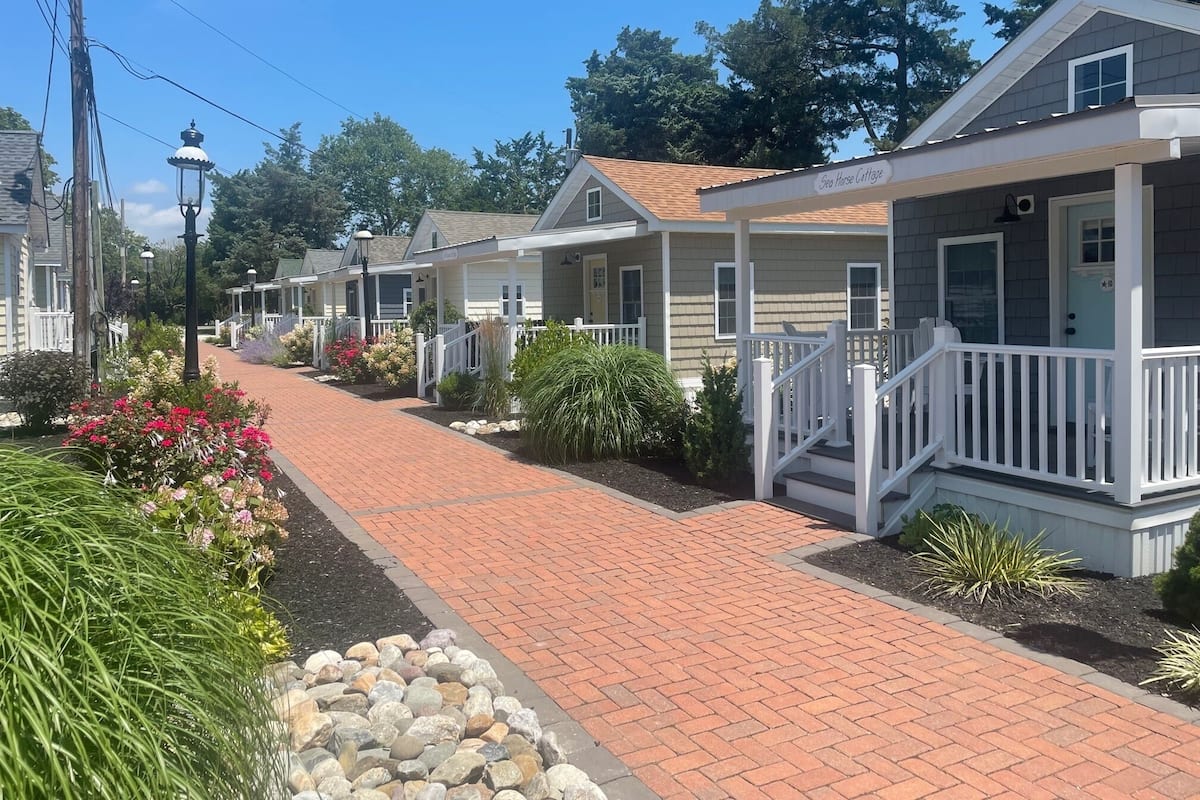 A row of single-story houses with front porches, a brick pathway, and a small garden area.