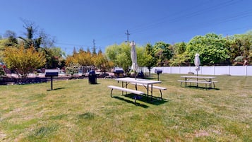 Un espacio al aire libre con mesas de picnic y sombrillas, rodeado de árboles y una valla.