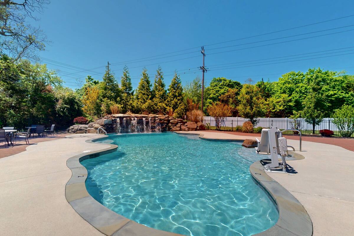 A swimming pool with a waterfall feature, surrounded by trees and outdoor seating.