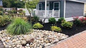 A residential house with a porch, a small garden with various plants and a rock border. - Coastal Estate (Cape May)