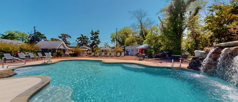 A clear swimming pool with lounge chairs and a waterfall feature.