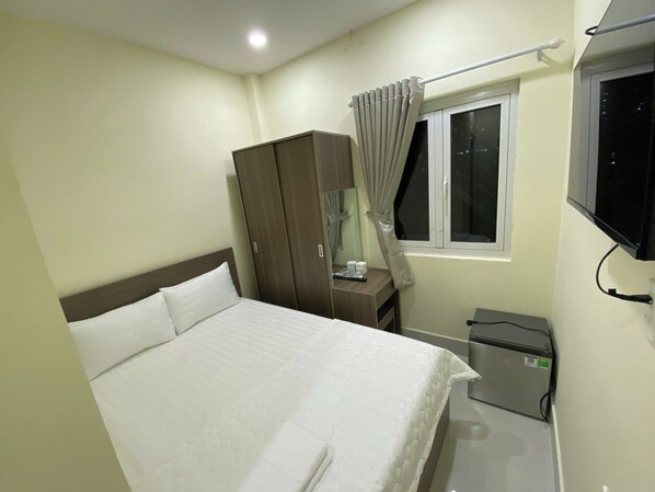 A hotel room with a bed, a wardrobe, a desk with a lamp, a TV mounted on the wall, and a window with curtains. - Khach San Gia Thanh (Ho Chi Minh City)