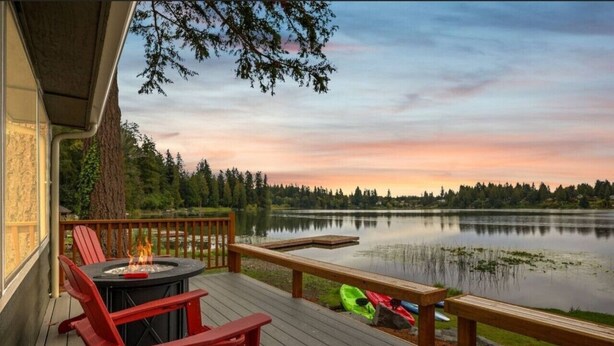 Une terrasse avec un foyer, des chaises rouges et une vue sur un lac au coucher du soleil.