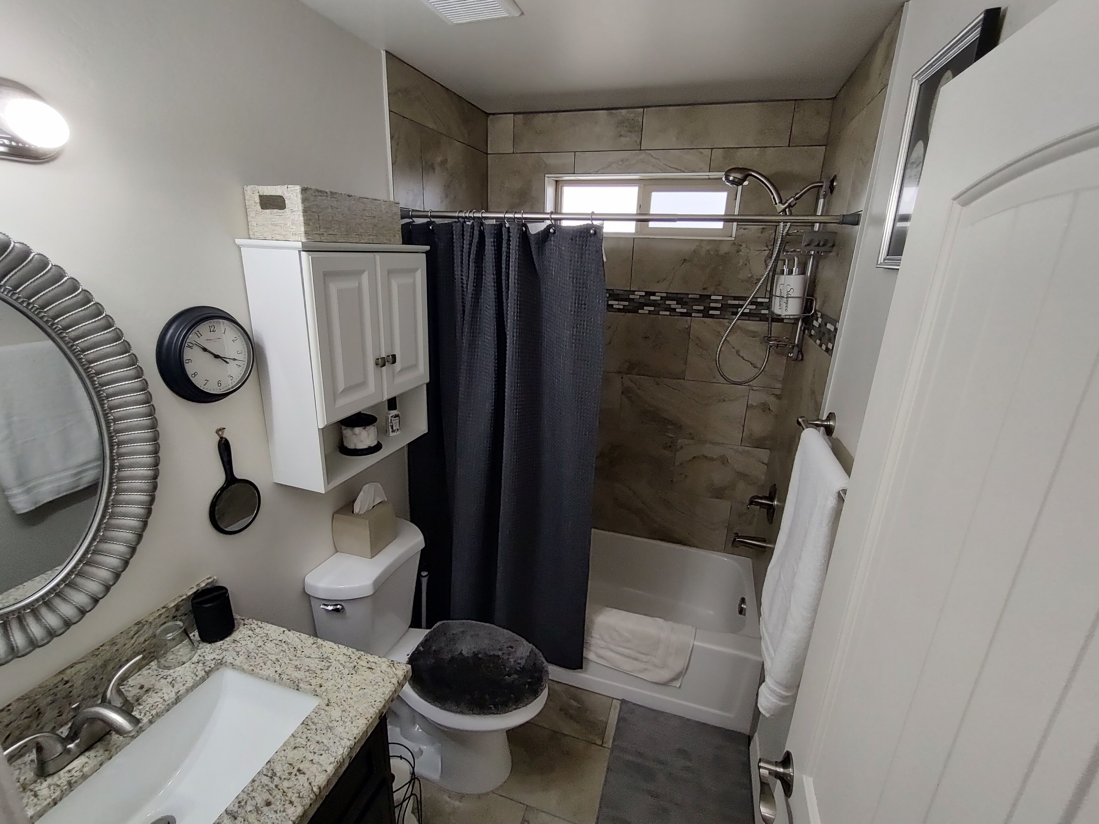 Une salle de bain équipée de toilettes, d’un lavabo, d’une douche et d’une horloge au mur.