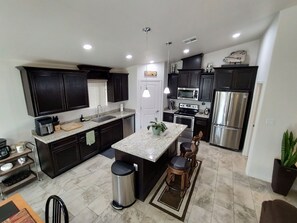 Una cocina moderna con armarios oscuros, electrodomésticos de acero inoxidable y una isla central con taburetes de bar.