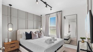 A modern bedroom with a large bed, bedside tables, a mirror, and a TV.
