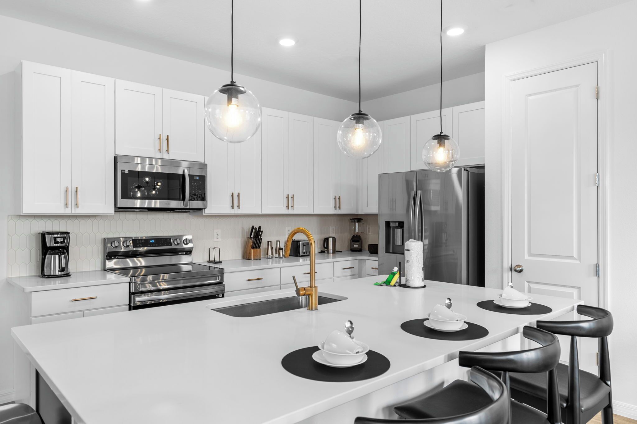 Une cuisine moderne avec des meubles blancs, des appareils en acier inoxydable et des tabourets de bar noirs.