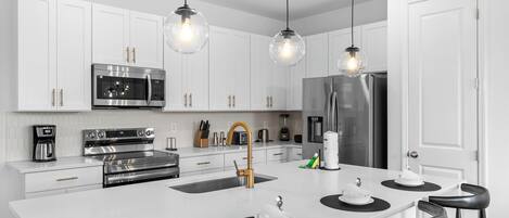 Une cuisine moderne avec des meubles blancs, des appareils en acier inoxydable et des tabourets de bar noirs.