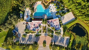 An aerial view of a resort with a central swimming pool, multiple guest buildings, and surrounding greenery.