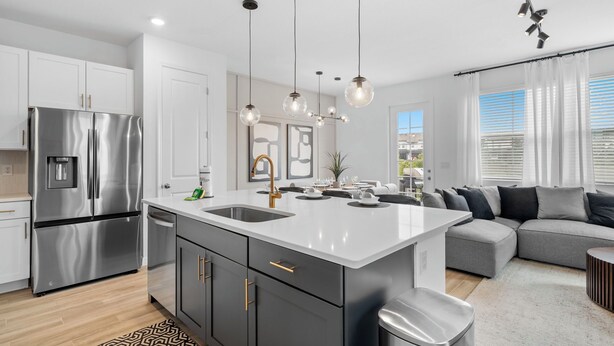 A modern kitchen with a stainless steel refrigerator, a white island with a sink, and pendant lighting.