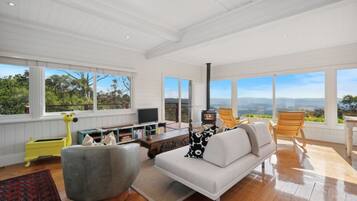 A spacious living room with a sofa, chairs, a fireplace, and large windows offering a scenic view.