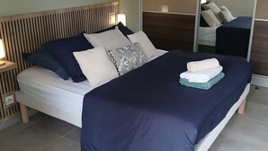 Un dormitorio moderno con una cama, mesita de noche, lámpara y un espejo grande.