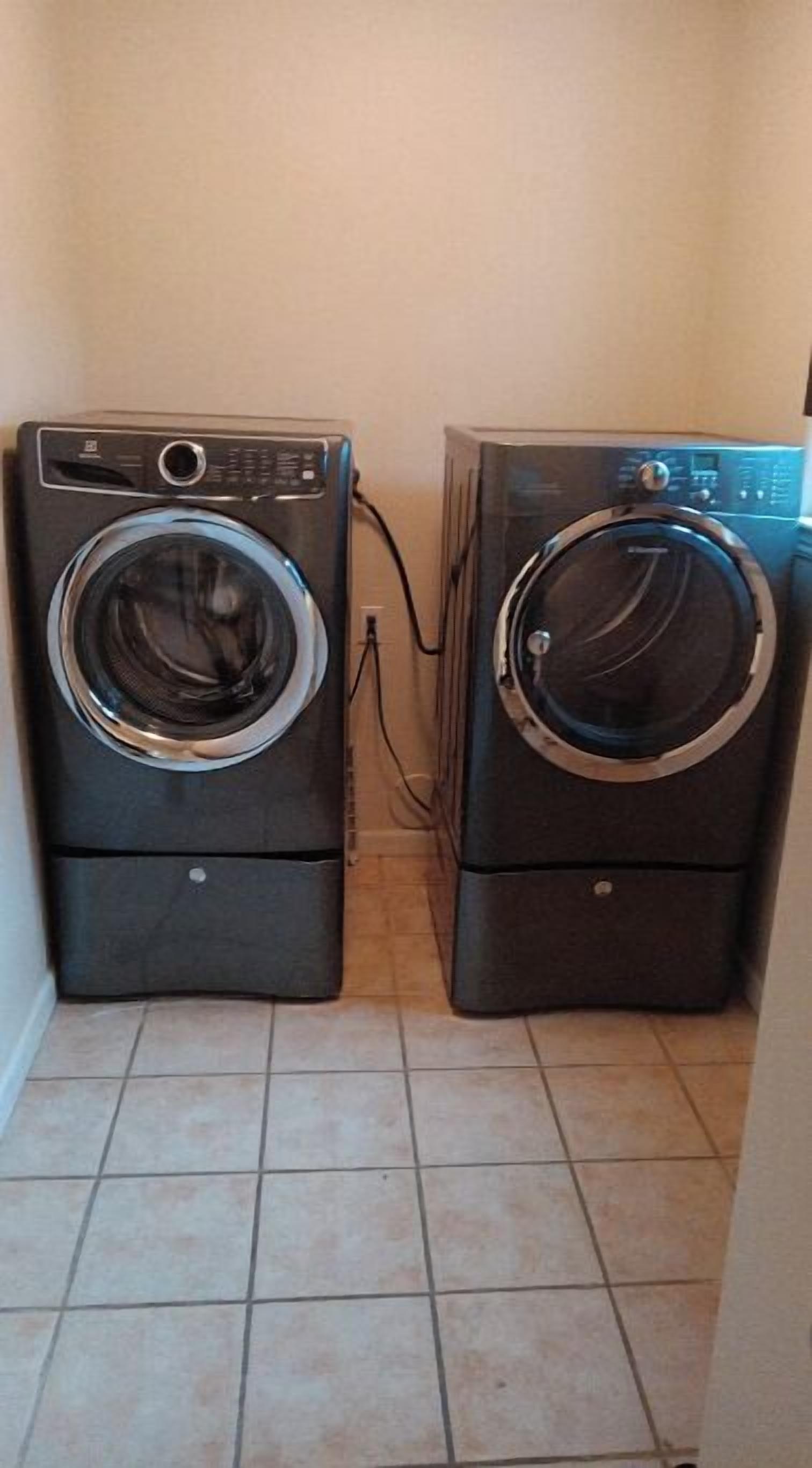 Two stacked front-loading washing machines in a small laundry room with tiled flooring.