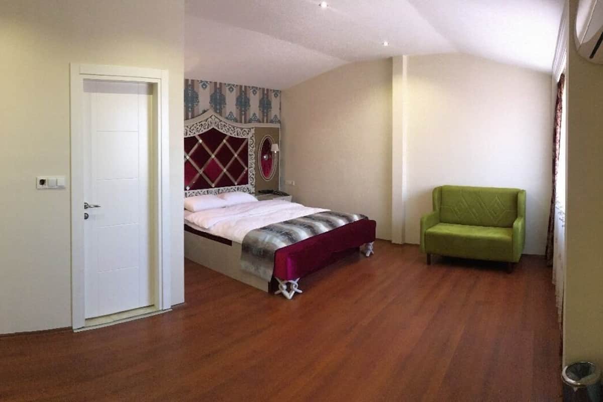 A bedroom with a bed, a green armchair, a mirror, and a door.