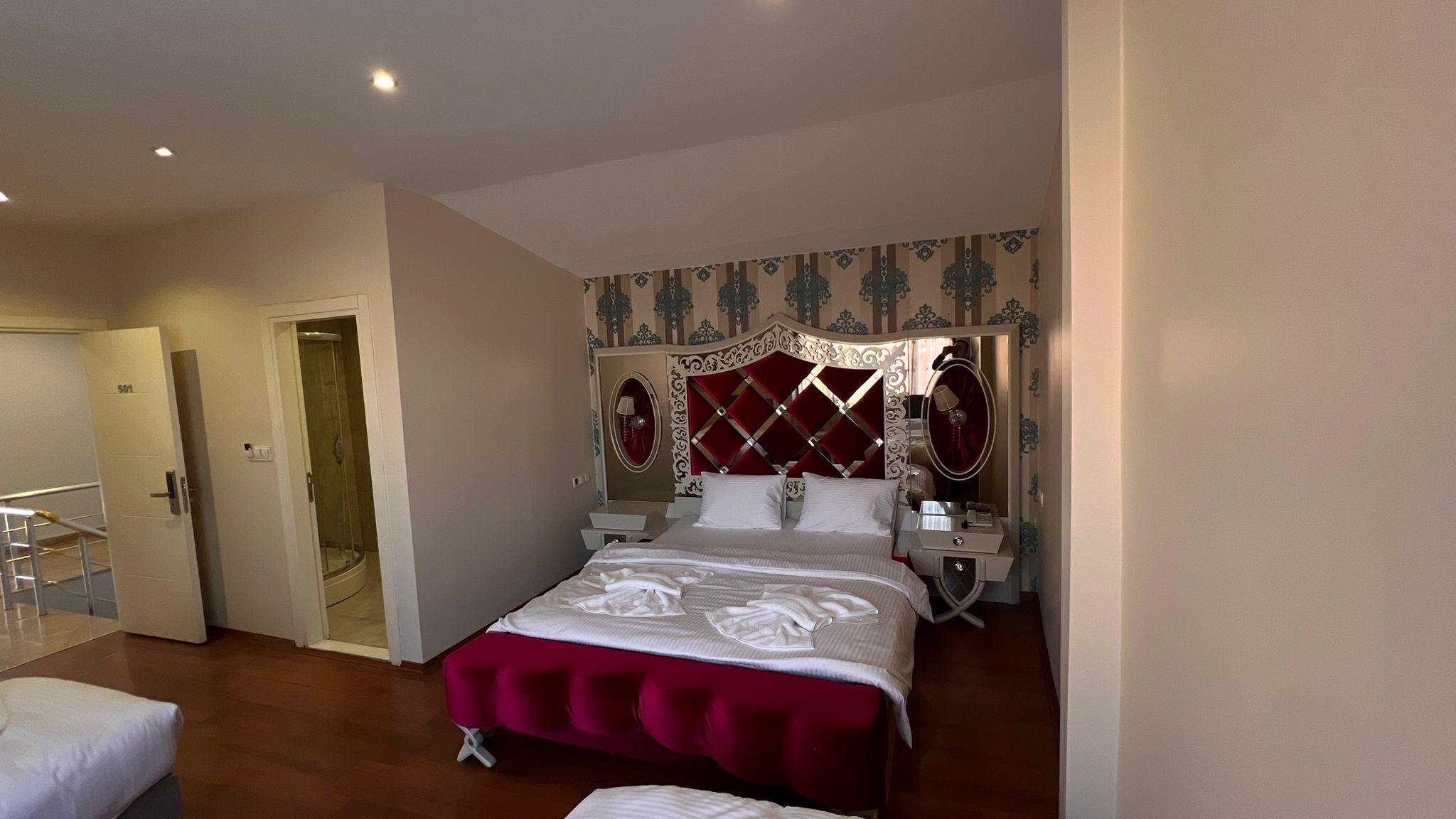 A hotel room with a large bed, a vanity with a mirror, a walk-in closet, and a shower.