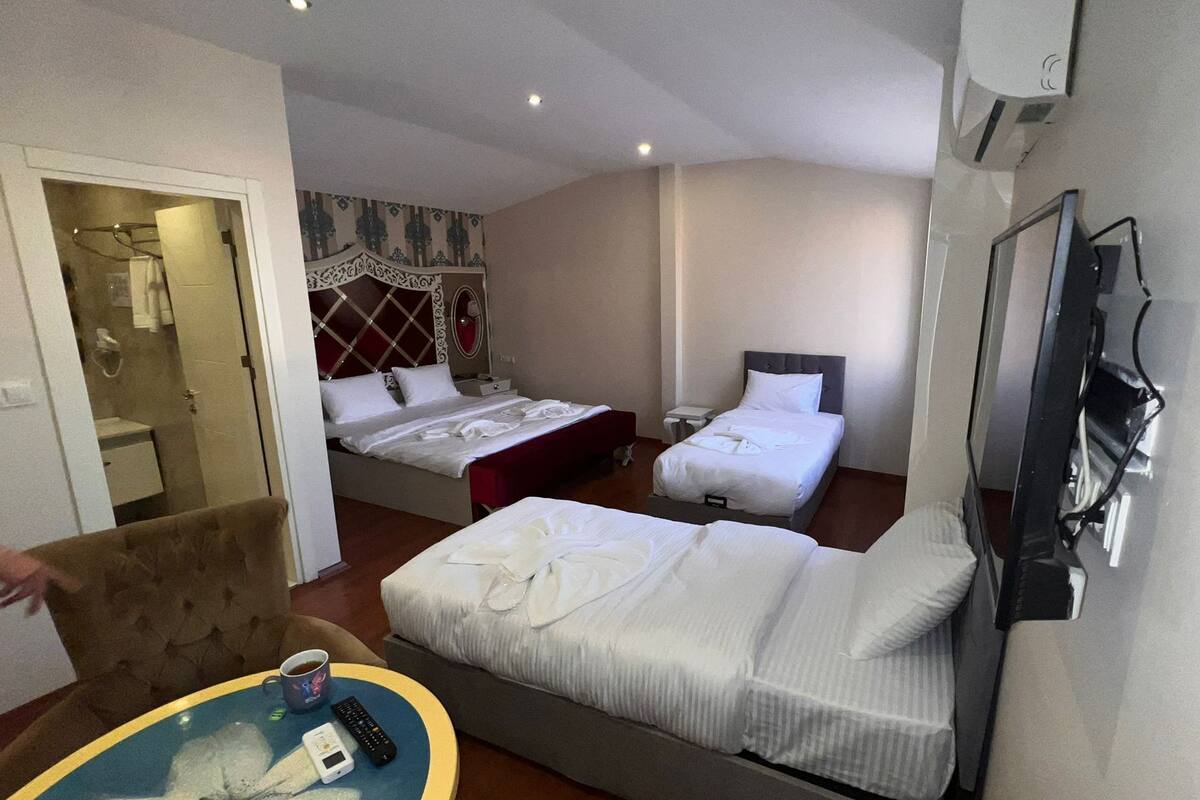 A hotel room with two beds, a TV, a coffee table with a remote and a cup, and a bathroom visible through an open door.