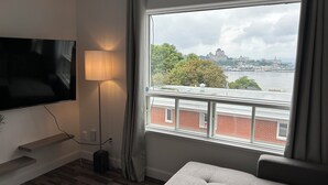 A modern living room with a flat-screen TV, a floor lamp, and a large window offering a city view. - What a View!!! Chateau, Balcony incredible view of the Chateau! Free parking! (Lévis)