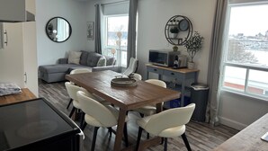 A modern living room with a dining area, grey sofa, white chairs, a wooden table, and a view of a snowy landscape through the window. - What a View!!! Chateau, Balcony incredible view of the Chateau! Free parking! (Lévis)