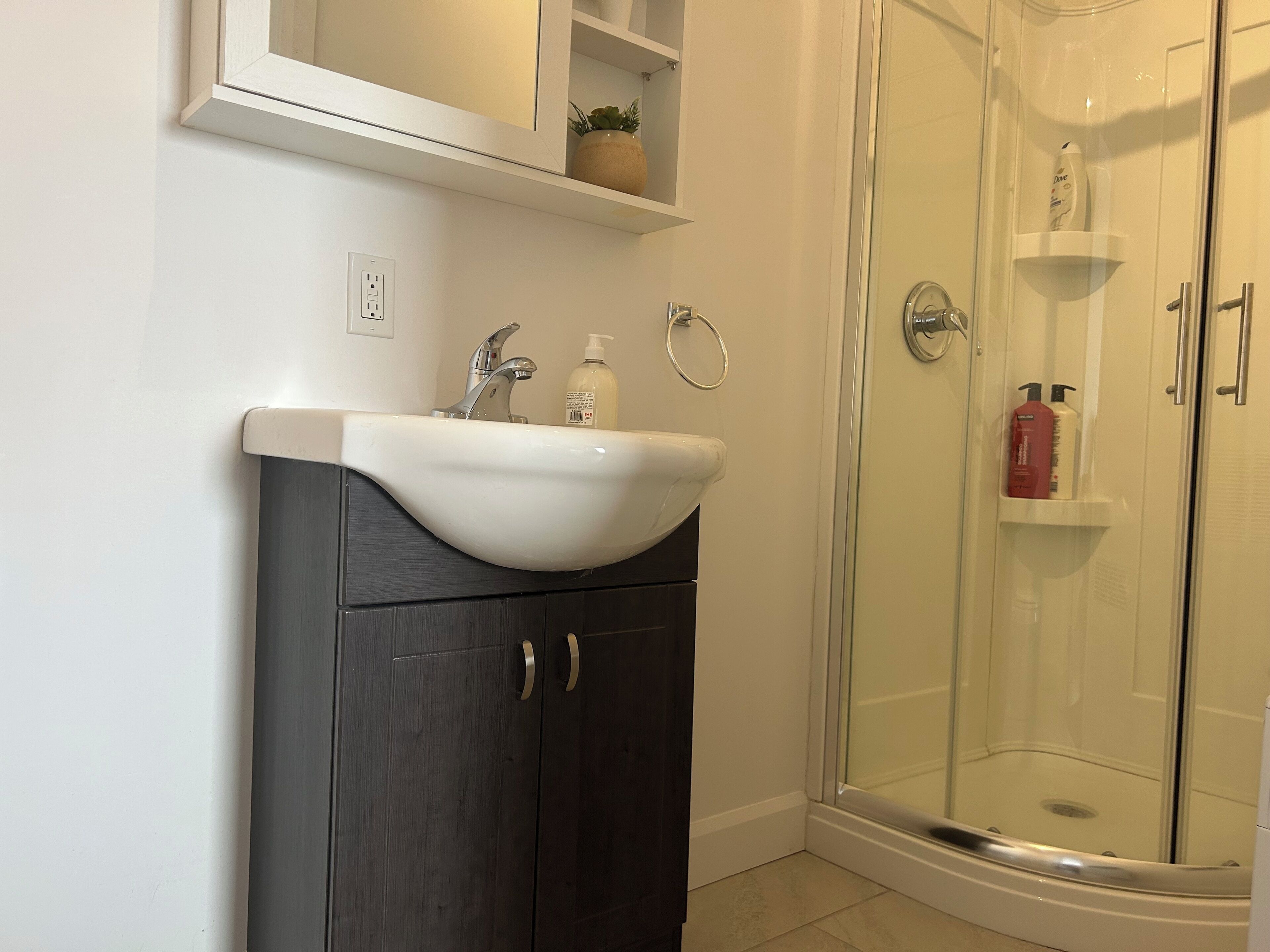A bathroom with a white sink, dark wooden cabinet, and a glass shower enclosure.