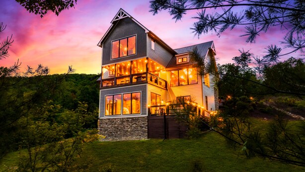 A two-story house with large windows and a stone facade, surrounded by trees and a grassy area. - Heated Pool/HotTub/Games/Fire/Sleep 20+ (Sevierville)