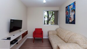 A living room with a flat-screen TV, a red chair, a beige sofa, a window with a view of trees, and a colorful painting on the wall. - Ad deactivated ad deactivated (Lapa de Baixo São Paulo)