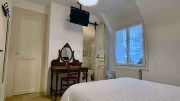 A bedroom with a bed, a dresser with a mirror, a chair, a ceiling fan, a window with curtains, and a wall-mounted television.