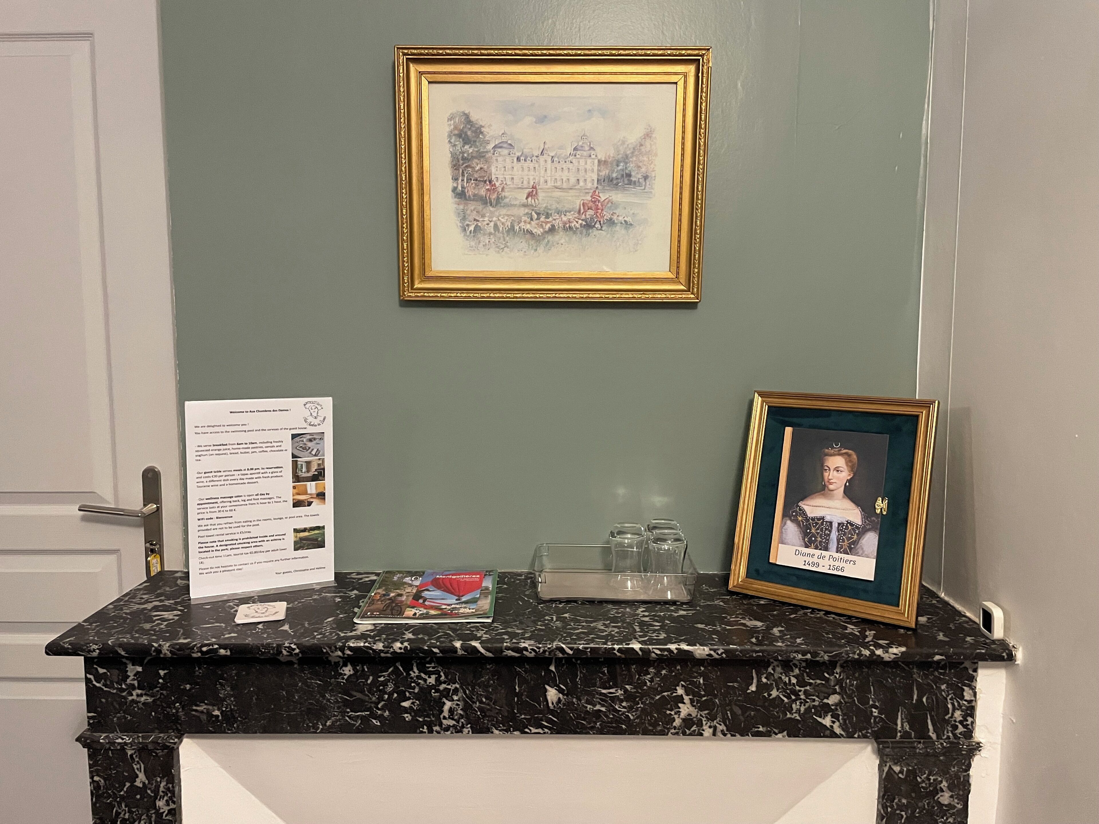 A reception desk with a framed painting, a framed portrait, and informational cards.