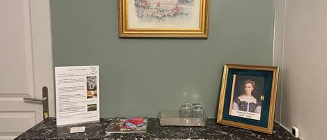 A reception desk with a framed painting, a framed portrait, and informational cards.