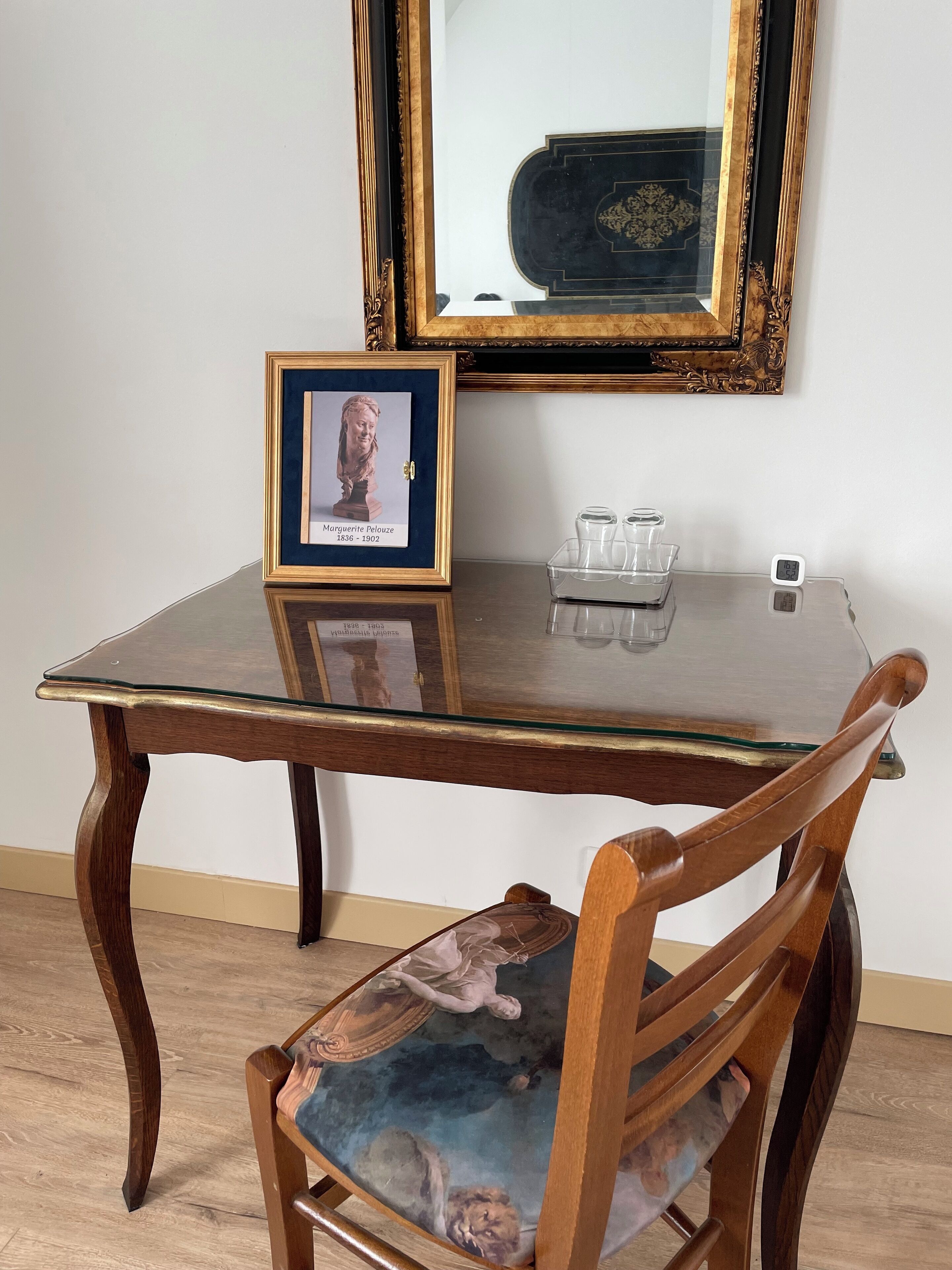 A wooden table with a glass top, a framed picture, and a small clock.