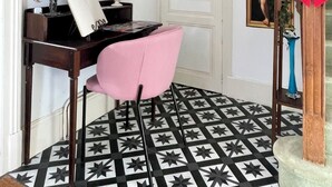 Ein Zimmer mit Schreibtisch, einem rosa Sessel, einem gemusterten Boden und einer Treppe mit roten Schleifen.