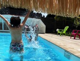 Une piscine dans laquelle une personne éclabousse l’eau, entourée d’une terrasse en bois et de deux chaises vertes.