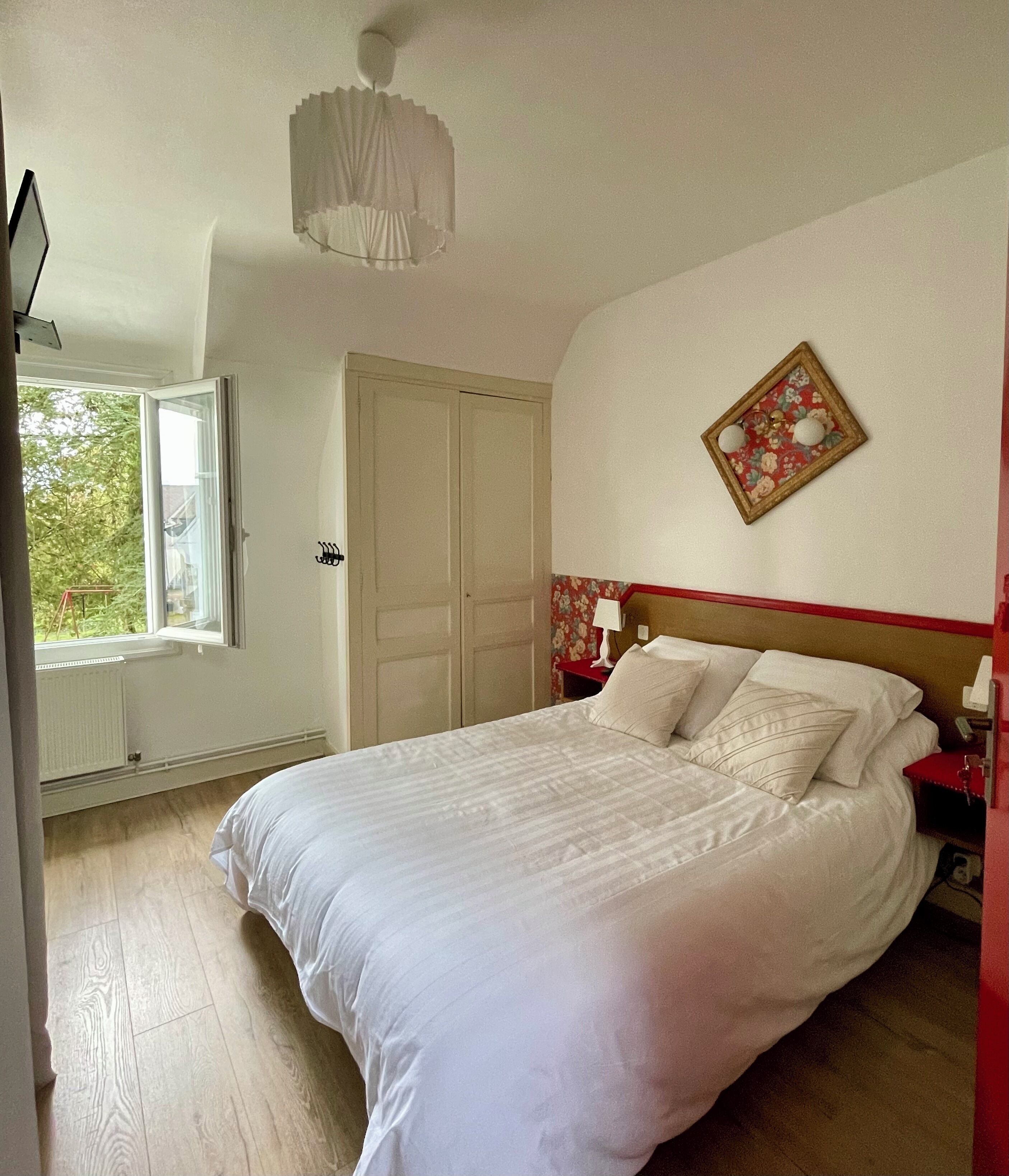 Un dormitorio con cama, ventana, puerta y lámpara fijada a la pared.